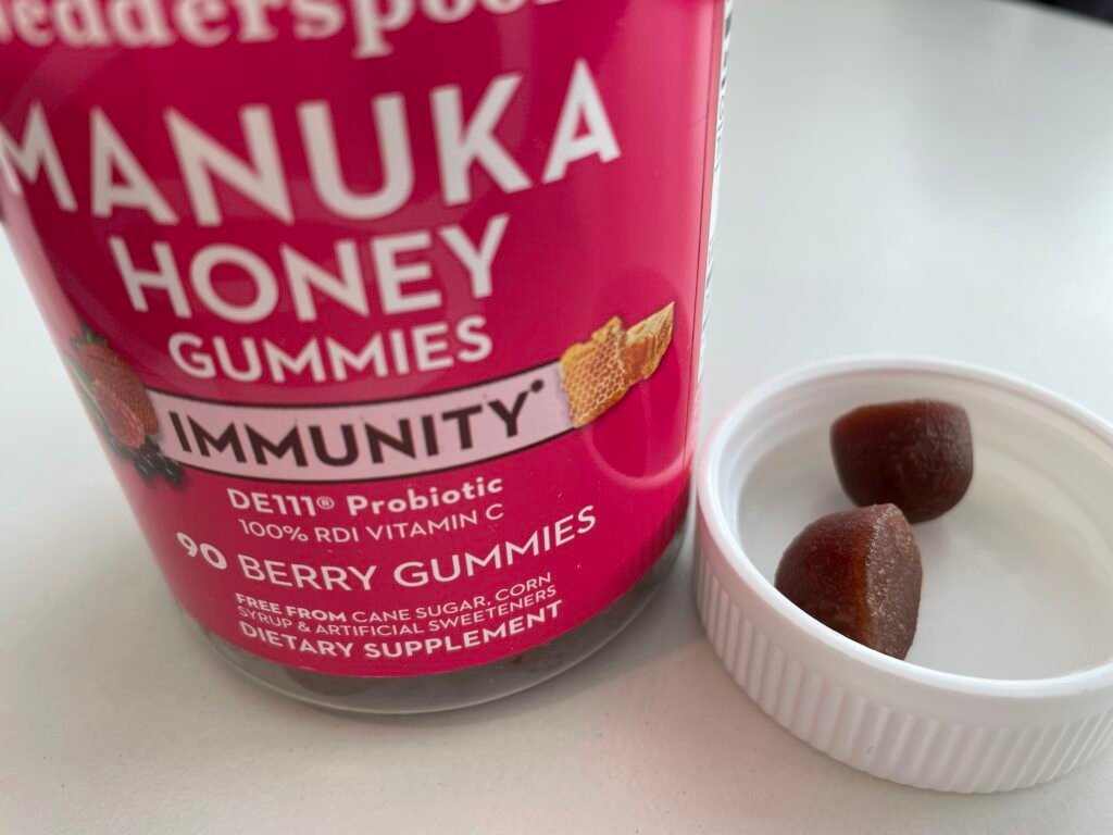 2 Manuka Honey Gummies in the jar lid up close with the full jar next to it on a white table top