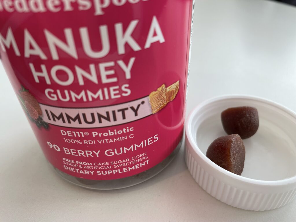 2 Manuka Honey Gummies in the jar lid up close with the full jar next to it on a white table top